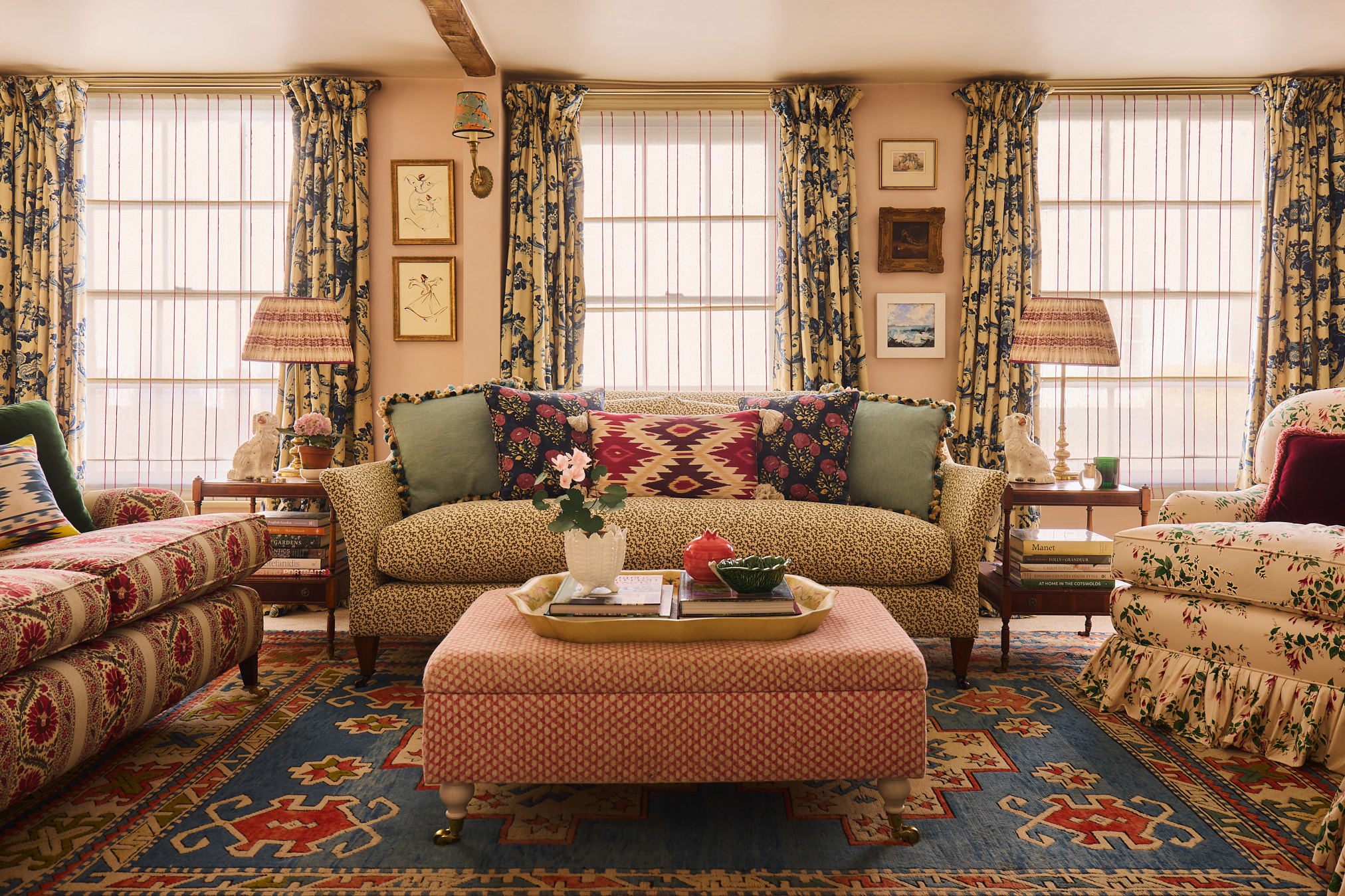 Sitting room with patterned sofa and cushions, kilim rug, red patterned ottoman and floral curtains in a Hampshire cottage
